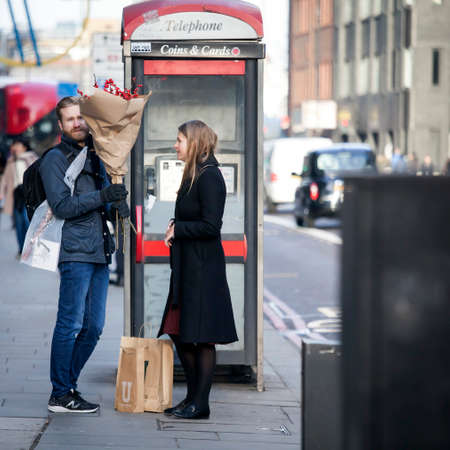 London, UK - December 22, 2017: A loving couple with red shrubbery stands near the phone booth near Liverpool streetのeditorial素材