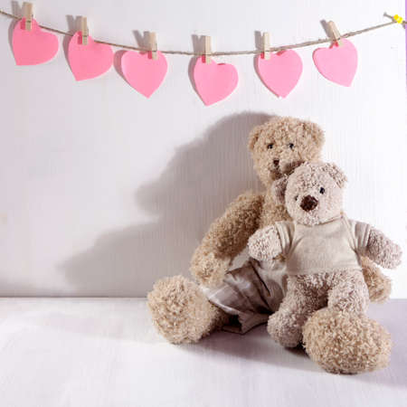 the Two teddy bears hug each other with . On wall the paper hearts hang. Valentine's Day greeting...