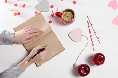 Hands of a woman who is going to draw by pencil in notebook. On the table there is a cup of tea with...