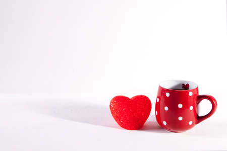 Red cup in a white point and red glass heart light is on a white wooden table. Copy spaceの写真素材