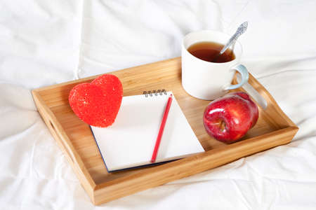 A tray with a cup of coffee, a notepad and a pencil stands on the bed