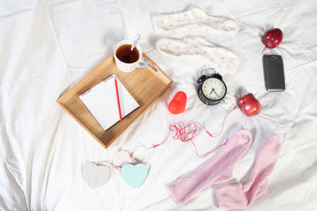 A tray with a cup of coffee, a notepad and a pencil stands on the bedの写真素材