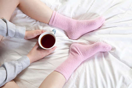 Hands holding a cup of coffee. You can see the legs in pink socks.の写真素材