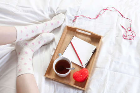 A tray with a cup of coffee, a notepad and a pencil stands on the bedの写真素材