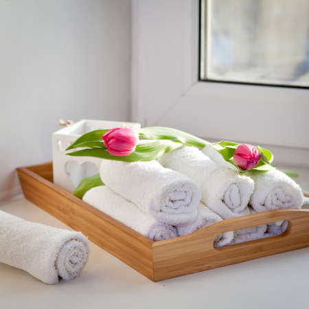 Rolled hand towels on a tray next to the lighted candles and a bouquet of tulips in the spa salonの写真素材