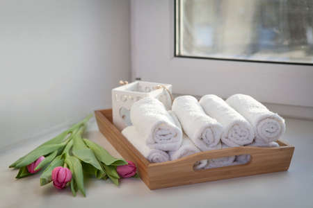 Rolled hand towels on a tray next to the lighted candles and a bouquet of tulips in the spa salonの写真素材