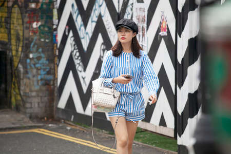 LONDON, ENGLAND - AUGUST 22, 2017 Fashionable young girl in blue striped overalls and a black cap goes down the street in east Londonのeditorial素材