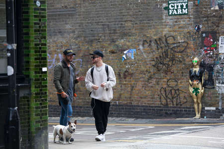 LONDON, ENGLAND - AUGUST 22, 2017 Two young men with a dog talking at the corner of the Brick Lane in East Londonのeditorial素材