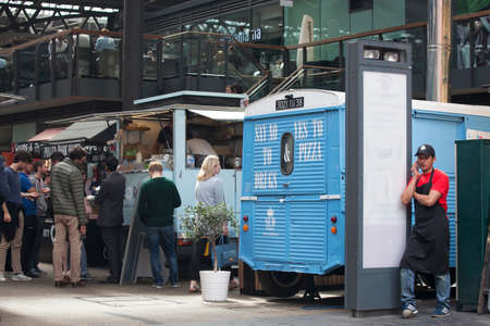 LONDON, ENGLAND - AUGUST 22, 2017 A pizza seller in a red T-shirt and cap talks on the phone, leaning on the van at Spitalfields marketのeditorial素材