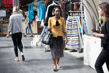 LONDON, ENGLAND - AUGUST 22, 2017 A woman in a yellow sweatshirt and a multicolored skirt goes through the marketのeditorial素材