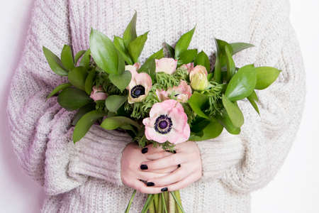 the girl in white wool sweater holds a wedding bouquet of anemones and Ruscus on the white backgroundの写真素材