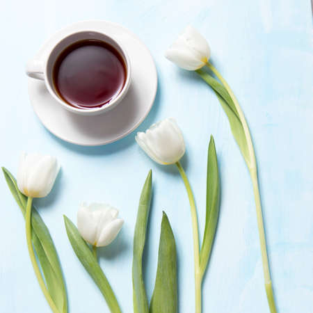 the white tulips and tea in the mug on blue wooden background as a cardの写真素材