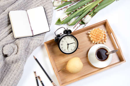 A tray with coffee, white tulips and willow stands on the bed. The alarm clock shows seven in the morning.の写真素材
