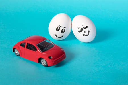 Hen eggs with painted faces. The concept. She leaned against himnear red car on a blue background.の写真素材