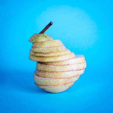 Pear, cut into thin slices, on a blue background. Conceptual postcard.の写真素材