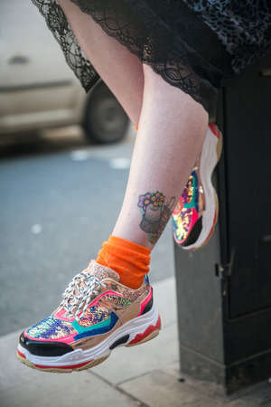 LONDON - FEBRUARY 15, 2019: Stylish attendees gathering outside 180 The Strand for London Fashion Week. Fragment of legs in sneakers with a flower tattooのeditorial素材