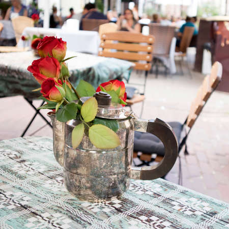 Vilnius, Lithuania, Red roses in a silver coffee pot on a table in a street cafe for decorationのeditorial素材