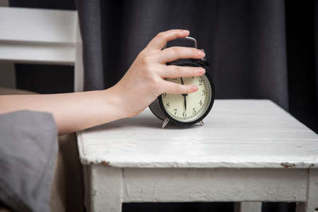 The girl, wrapped in a grey blanket, puts out her hand to turn off the alarm. There is six hours on...