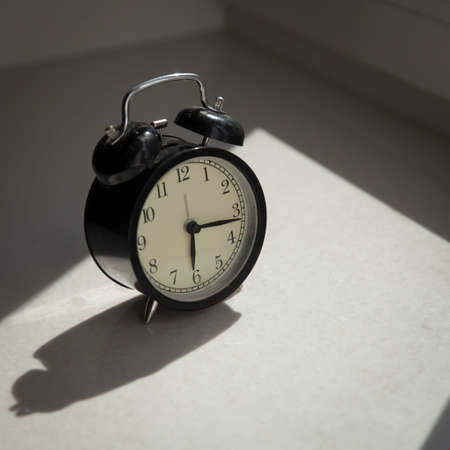 The alarm clock is on the window. It shows time at a quarter to six.の写真素材