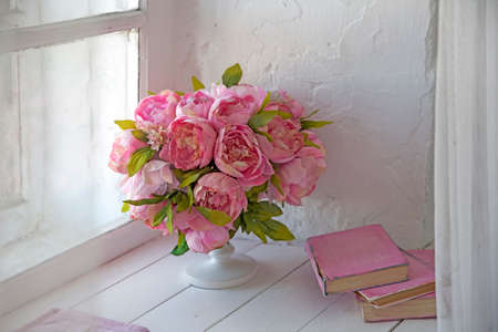 A bouquet of orchids, peonies, roses in a ceramic vase and a stack of booksの写真素材