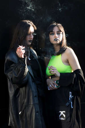 LONDON, ENGLAND - September 15, 2019 Stylish attendees gathering outside 180 Strand for London Fashion Week. Two girls dressed in black and green gothic costumes smoke by the wallのeditorial素材