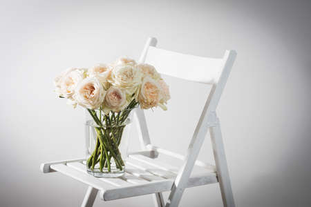 A bouquet of white and pink roses on a wooden chair against a white wall with empty space for writing.の写真素材