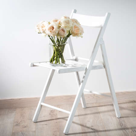 A bouquet of white and pink roses on a wooden chair against a white wall with empty space for writing.の写真素材
