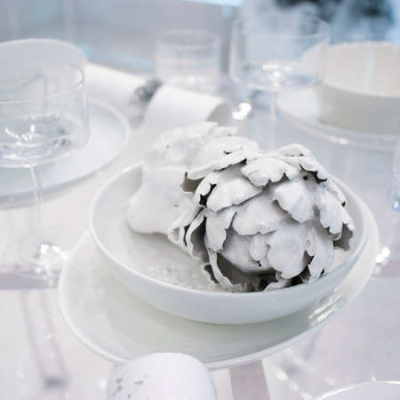 Christmas festive table decoration in white colors. Painted white artichoke in a ceramic plateのeditorial素材