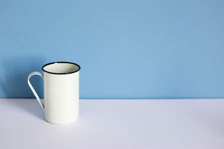 white enameled high mug on a white and blue background. Copy spaceの写真素材