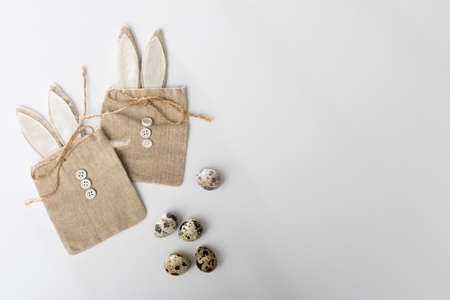 Quail eggs on a white dish. decoration. Packing canvas gift bags with buttons in the form of a hare on a white background. Easter card. Copy spaceの写真素材