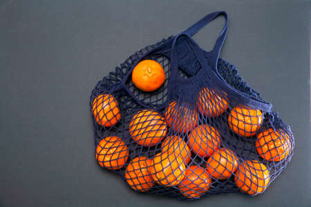 Blue string bag with tangerines on a pink paper backgroundの写真素材