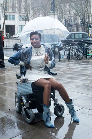 LONDON, UK- febryary 15 2020: Fashionable people on the street . Street style. Girl in a wheelchair with an umbrellaのeditorial素材