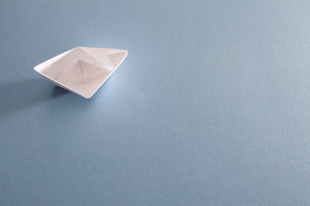 White paper handmade origami boat on the blue background. Copy space for your text. Theme of...