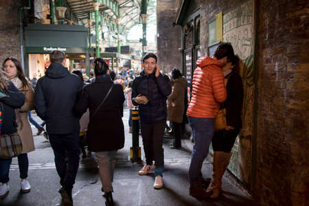 London, UK - 12 March 2020 The crowd goes under the bridge at Borough Market. Loving couple kisses leaning to the wall.のeditorial素材