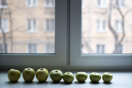 A row of green apples lies on a stone windowsill on the window. Copy space.の写真素材