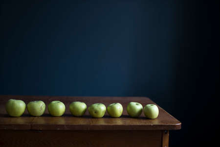 A row of green apples lie on a wooden table opposite a dark blue wall. Copy space.の写真素材