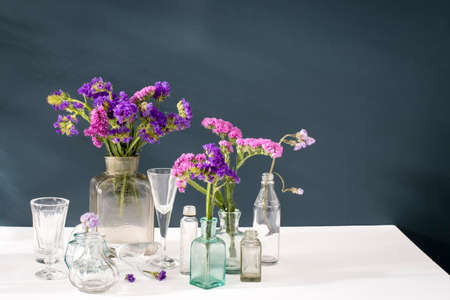 A bouquet of limonium in the transparent vase and a set of small bottles on a dark blue background.の写真素材