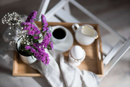 Bouquet of limonium and gypsophila on a tray. Morning tea with milk jug with milk, an egg in a stand, on a tray on a chair. Breakfast. Focus on Lemoniumの写真素材