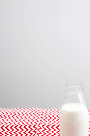 An open bottle of milk is on a red and white tablecloth in a zigzag on the table against the background of a gray wall in the kitchen. Copy spaceの写真素材
