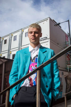 London, UK - 15 February, 2020, Fashionable people on the street . Street style. a blond man in a light blue jacket, a multi-colored white-flowered shirt, black trousers poses opposit blue sky.のeditorial素材