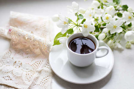 White cup of morning espresso with a blossoming apple tree branch on a stone surface of a table with...