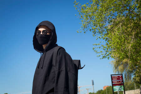 Young man with orange dyed hair in a black hoodie with trousers and sports boots in a protective...