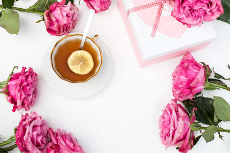 a bouquet of red roses surrounds a cup of tea with lemon and saucer. Circle. Box for gift with heart...