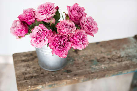 Bouquet of red roses in a tin bucket on a white wall background on a wooden wrecked surface of the bench. Copy spaceの写真素材