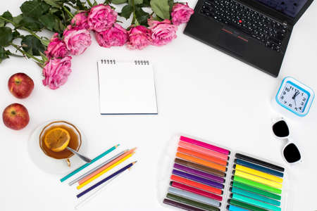 Laptop, notebook, felt-tip pens, watches, sunglasses, a cup of tea with lemon, pencils and a bouquet of red roses on the office desk. Frame.Copy spaceの写真素材