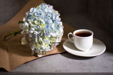 A branch of green pastel hydrangeain with white cup of coffee on a on a gray craft vintage background. Copy spaceの写真素材