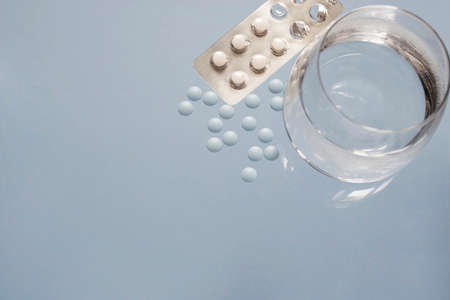 Close up of teblets pills spilling from pill bottle with a glass of water on blue background. Copy spaceの写真素材