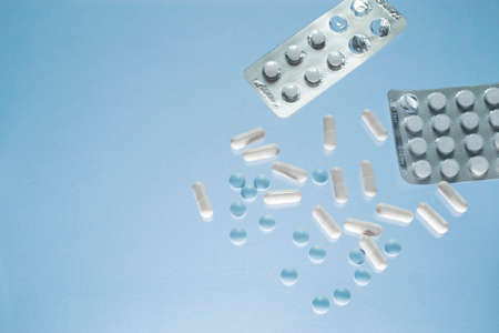 Close up of teblets pills spilling from pill bottle with a glass of water on blue background. Copy...