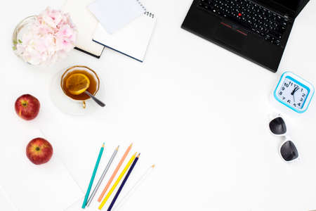 Laptop, notebook, felt-tip pens, watches, sunglasses, a cup of tea with lemon, pencils and a bouquet of hydrangea on the office desk. Frame. Copy spaceの写真素材