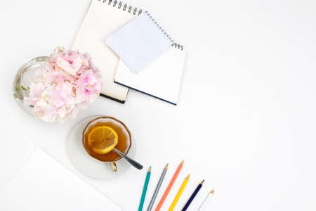 Laptop, notebook, felt-tip pens, watches, sunglasses, a cup of tea with lemon, pencils and a bouquet of hydrangea on the office desk. Frame. Copy spaceの写真素材